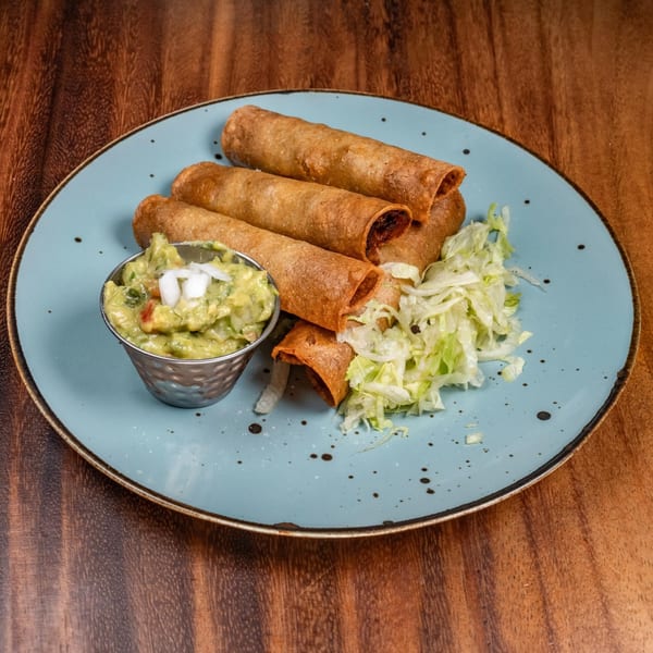 Crispy taquitos with guacamole and shredded lettuce on a light blue plate.