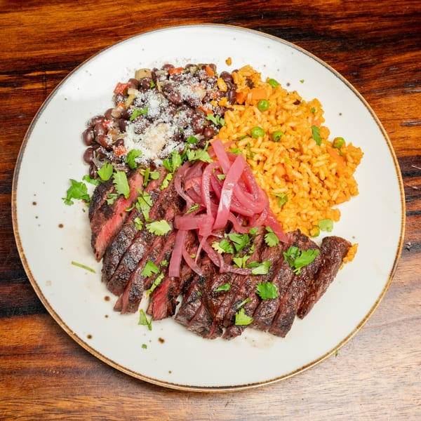Sliced steak with pickled red onions, cilantro, black beans, and orange rice on a white plate.