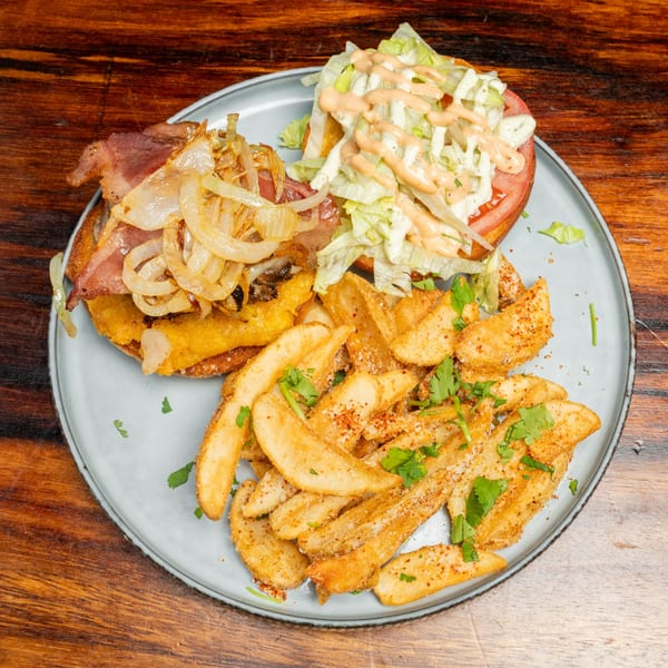 Open-faced burger with bacon, caramelized onions, lettuce, tomato, and sauce, served with seasoned potato wedges.