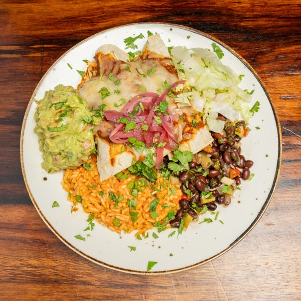 A plate of enchiladas with melted cheese, rice, black beans, guacamole, and shredded lettuce.