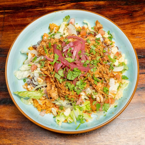 A colorful bowl of shredded chicken, rice, lettuce, corn, and pickled red onions on a wooden table.