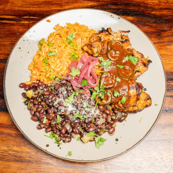 Grilled chicken with mole sauce, rice, black beans, and pickled onions on a plate.