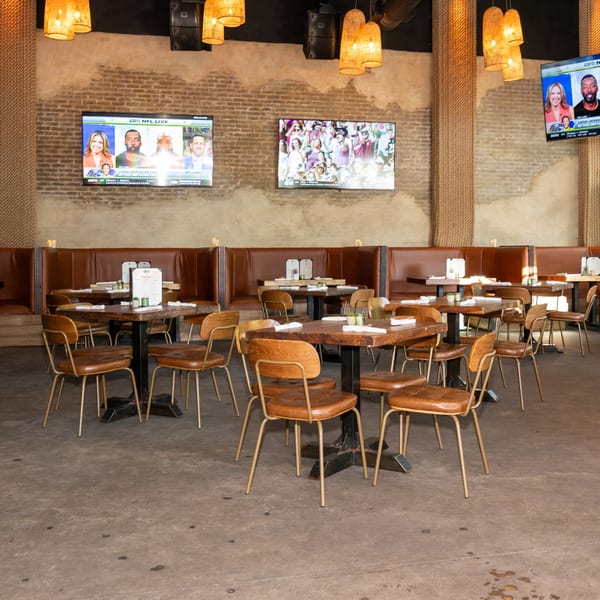 Restaurant interior with wooden tables, brown leather chairs and booths, and TVs showing sports.
