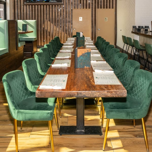 Long wooden dining table with green velvet chairs and menus set in a restaurant.