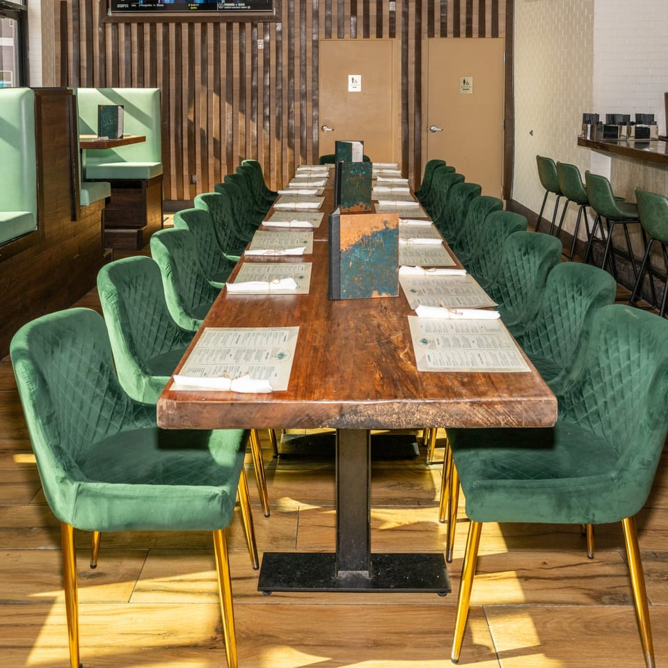Long wooden dining table with green velvet chairs and menus set in a restaurant.